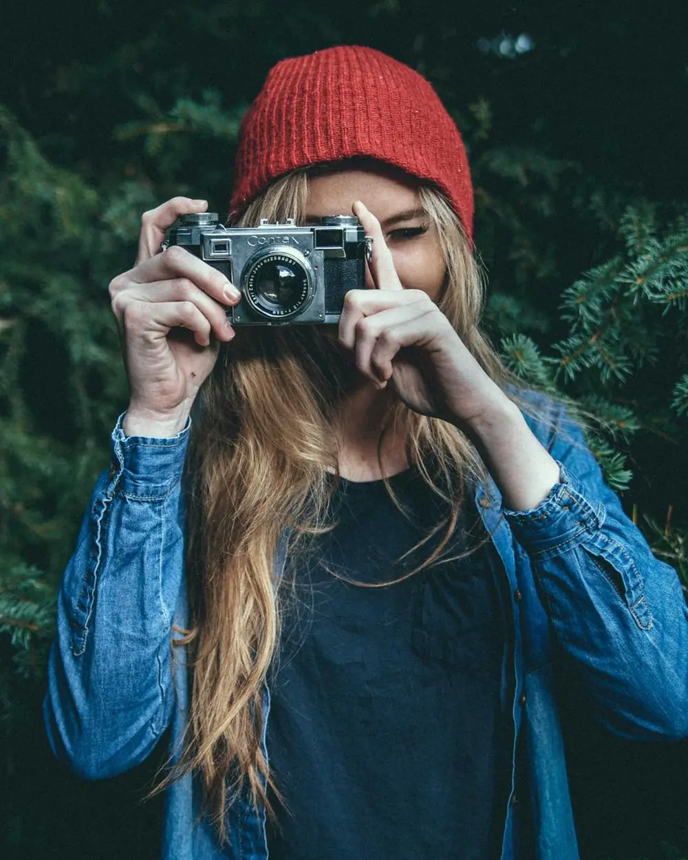 Woman in a red beanie holding a camera in a forest