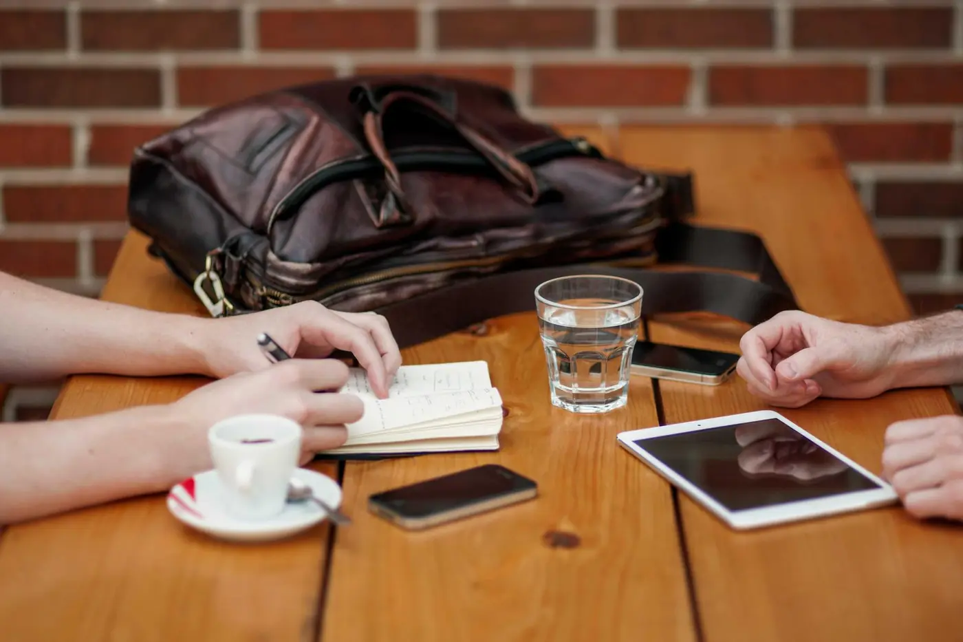 Two people reviewing notes and a tablet over coffee at a wooden table