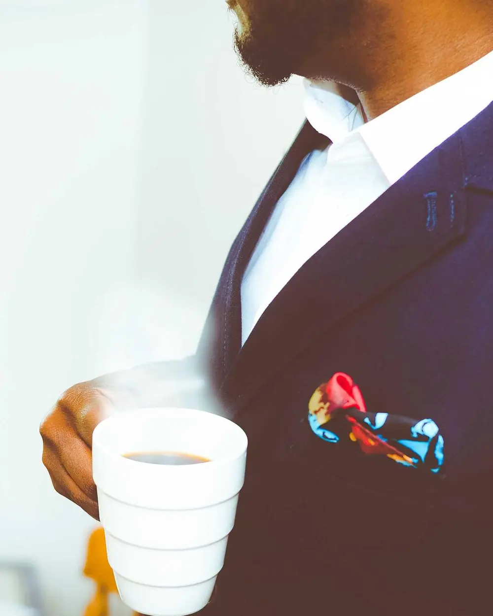 Man in a navy suit jacket holding a coffee cup