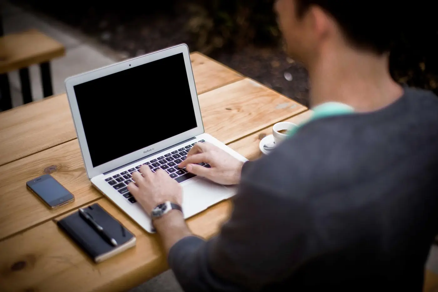 Person typing on a laptop at a wooden desk with a phone and coffee
